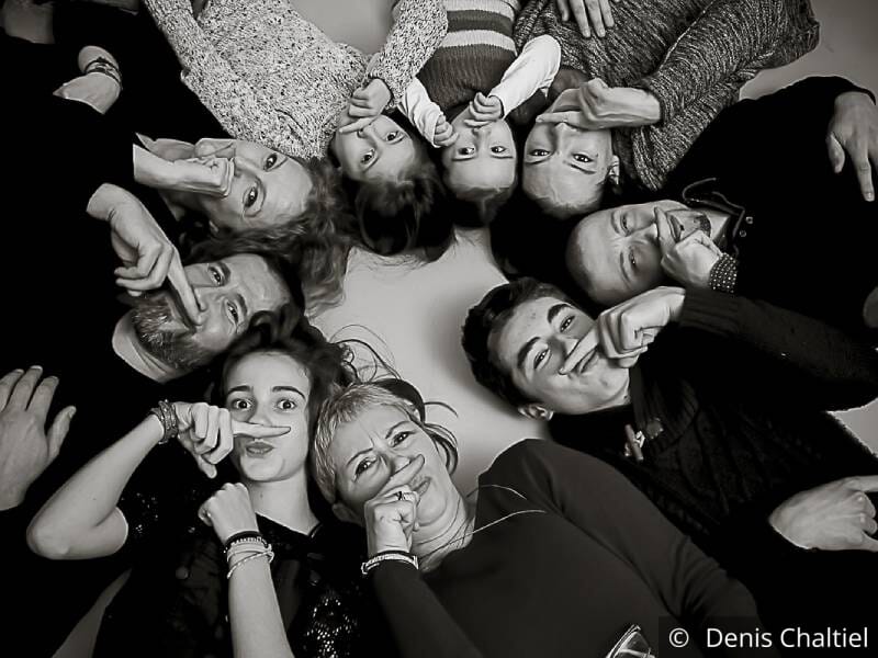 Photo de famille en noir et blanc, les personnes sont allongées en cercle et ont un doigt sous leur nez pour la pose.